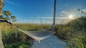 Eine Hängematte zwischen Bäumen an einem Sandstrand, strahlender Himmel und Sonne.