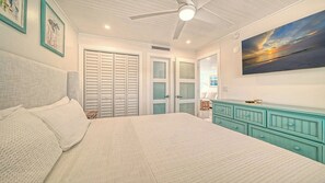 A bedroom with a bed, a ceiling fan, a painting, and a dresser.
