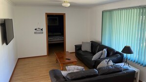 A living room with a black leather sofa, a wooden coffee table, and a TV mounted on the wall.