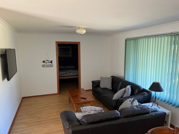 Una sala de estar con un sofá de cuero negro, una mesa de centro de madera y un televisor montado en la pared.