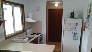 A compact kitchen with a stove, sink, and refrigerator, wooden stools, and a window.