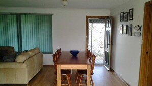 A dining area with a wooden table and chairs, a blue bowl, a beige sofa, and a door leading outside.