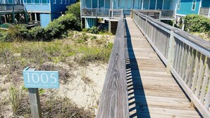Un paseo marítimo de madera que conduce a una casa frente a la playa, con un letrero que dice '1005 Rey del Mar'.