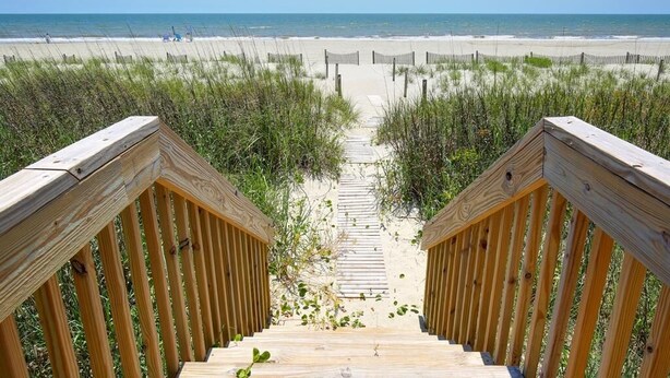 A wooden staircase leading to a beach with a clear view of the ocean and sand dunes. - Experience oceanfront bliss at Summer Sandcastle, a spacious 5BR home in Holden Beach! (Holden Beach)