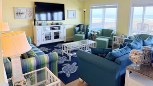 A living room with a television, seating, a ceiling fan, and a view of the ocean. - Experience oceanfront bliss at Summer Sandcastle, a spacious 5BR home in Holden Beach! (Holden Beach)