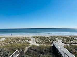 Une plage avec une promenade en bois menant à un bâtiment, un ciel dégagé et une mer calme.