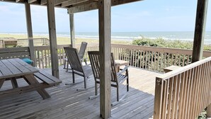 A wooden deck with chairs and a table overlooking the beach. - Experience oceanfront bliss at Summer Sandcastle, a spacious 5BR home in Holden Beach! (Holden Beach)