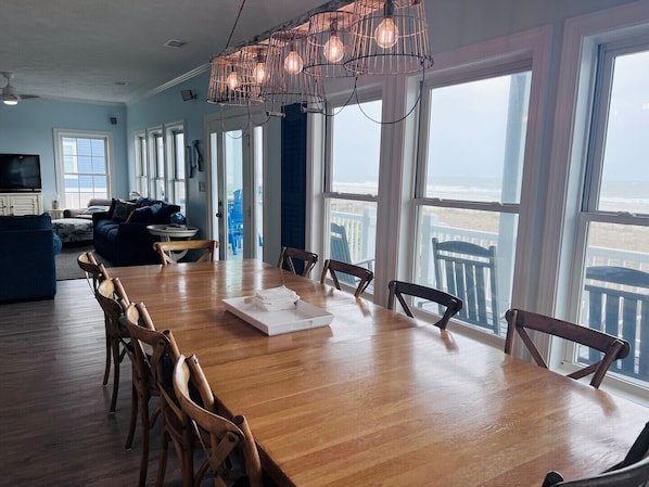 Relax in this stylish living area with a large dining table, comfortable seating, and a TV, offering a view of the beach.