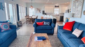 Een moderne woonkamer met blauwe banken, een houten salontafel en een eethoek met een tafel en stoelen.