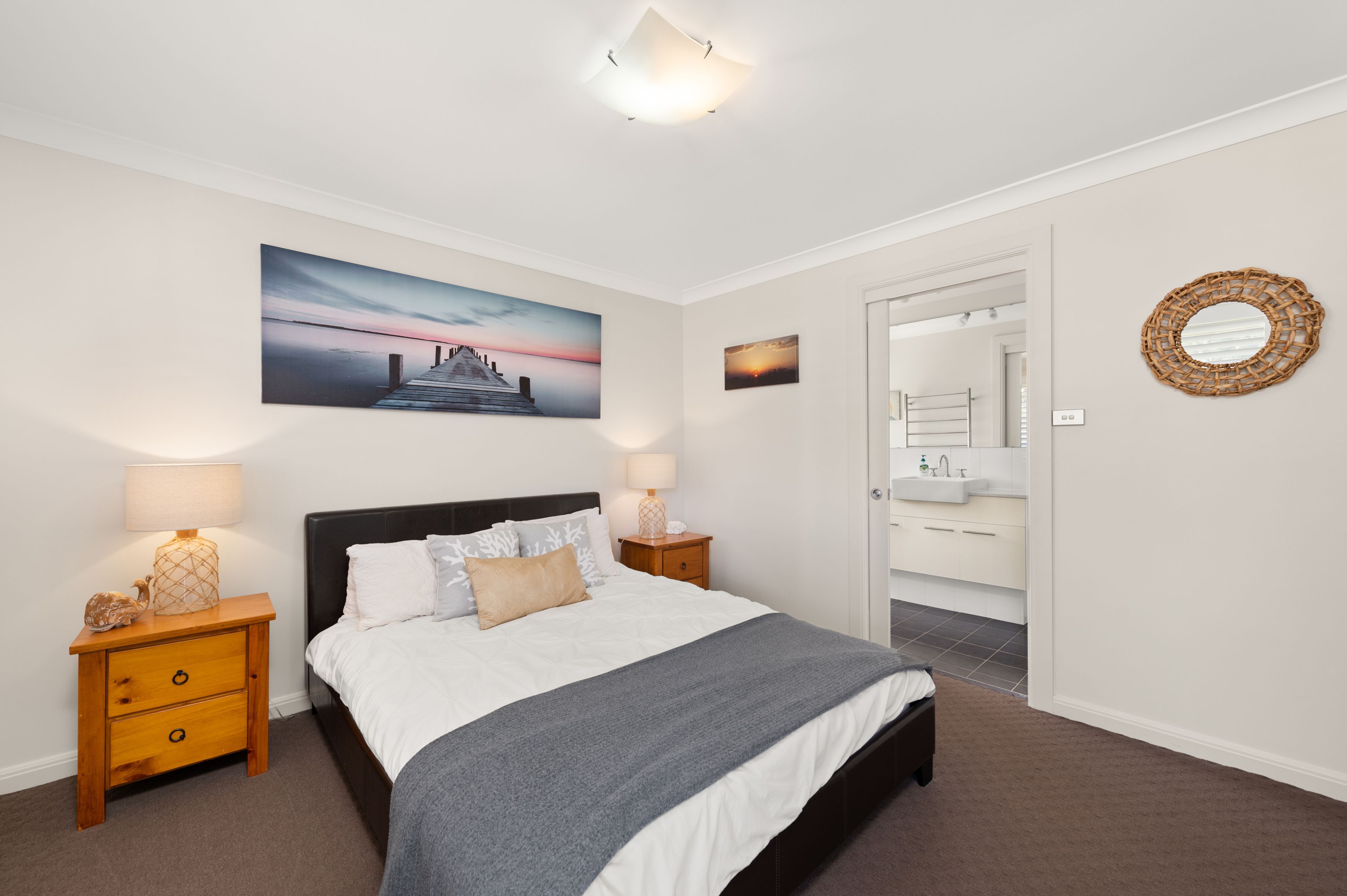 A bedroom with a bed, two bedside tables, a nightstand, a wall-mounted mirror, and a door leading to a bathroom.