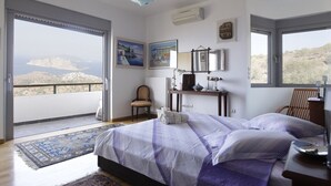 Quarto com uma cama grande, uma escrivaninha e uma cadeira. Vista do campo pela janela.