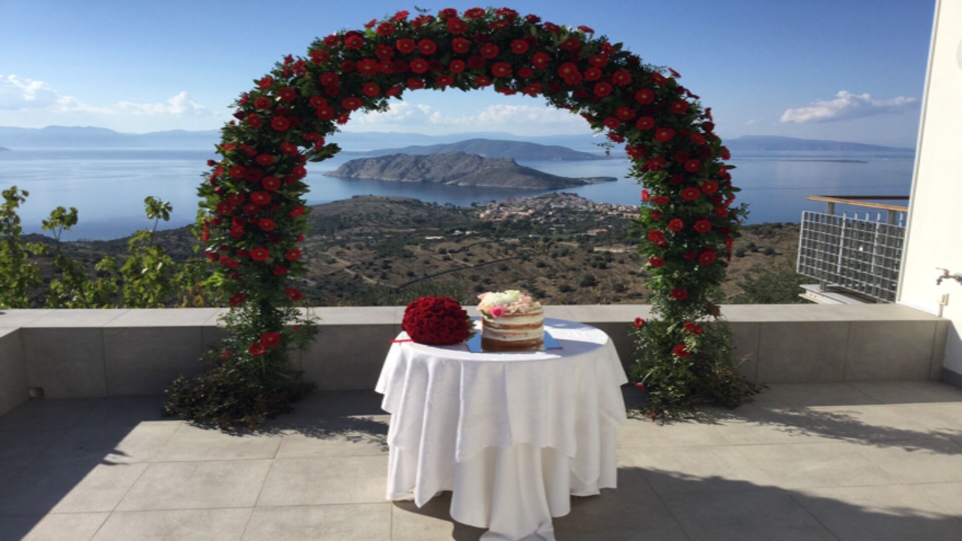 A wedding setup with a table under a floral arch, overlooking a scenic landscape.