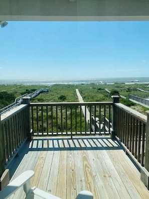 Une terrasse en bois dotée d’une rambarde, offrant une vue sur un paysage côtier sous un ciel dégagé.