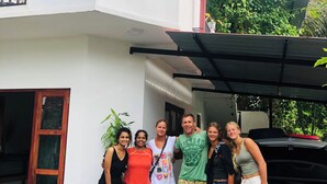 A group of people standing in front of a modern house with a covered porch and a car parked nearby.