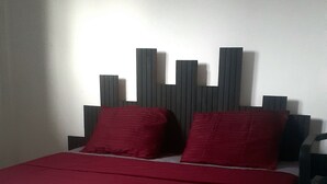 A bed with a red bedspread and two red pillows, a wooden headboard, and a nightstand with a lamp.