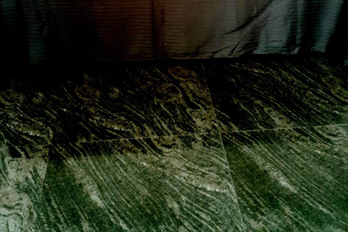 Ein Bett mit brauner Bettdecke und Kopfteil, ein Nachttisch mit Lampe sowie eine Kommode mit kleinem Schrank.