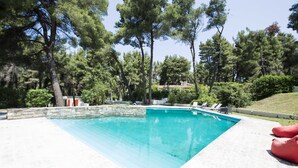 Piscina rectangular con un muro de piedra, rodeada de árboles y un césped.