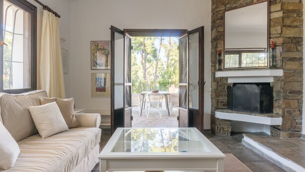 Una sala de estar con un sofá color beige, una mesa de centro de vidrio, una chimenea y vistas al exterior.