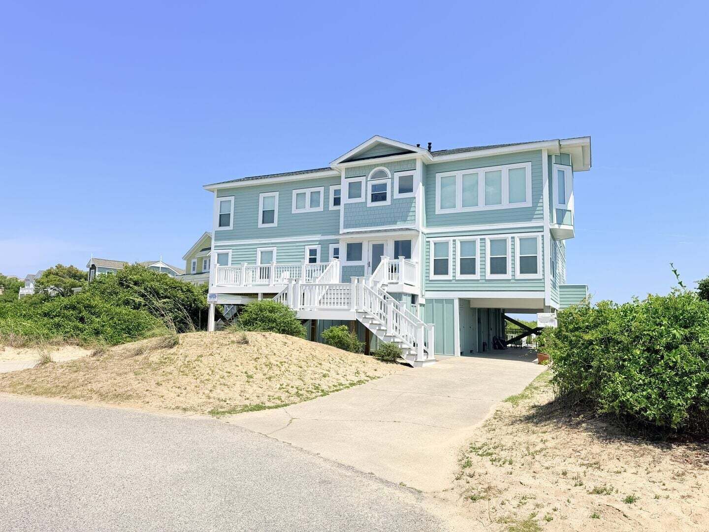 Une maison à plusieurs étages située en bord de mer, dotée d’un balcon imposant et d’un escalier menant à l’entrée.