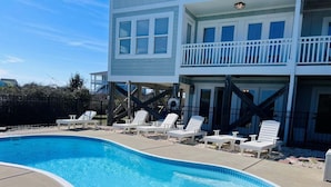 A swimming pool with lounge chairs, a wooden deck, and a two-story building with balconies.