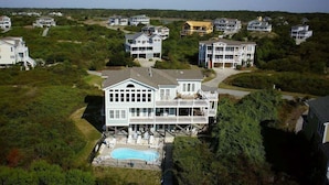 A large house with a pool, surrounded by dense greenery and other houses.