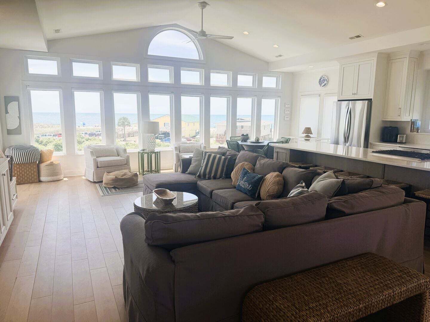 A spacious living room with a large sectional sofa, a dining area, and a kitchen with a view of the ocean.