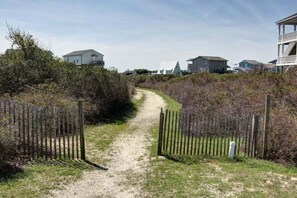 Un chemin de gravier mène à une zone délimitée par une grille, avec des maisons en arrière-plan.