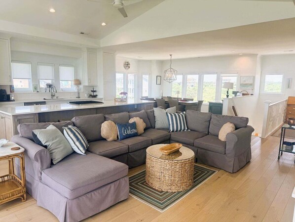 A spacious living area with a large sectional sofa, a round woven coffee table, and a kitchen in the background.