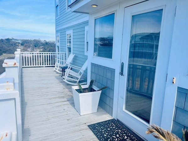 A blue building with a wooden deck, white railings, and a door with glass panels.