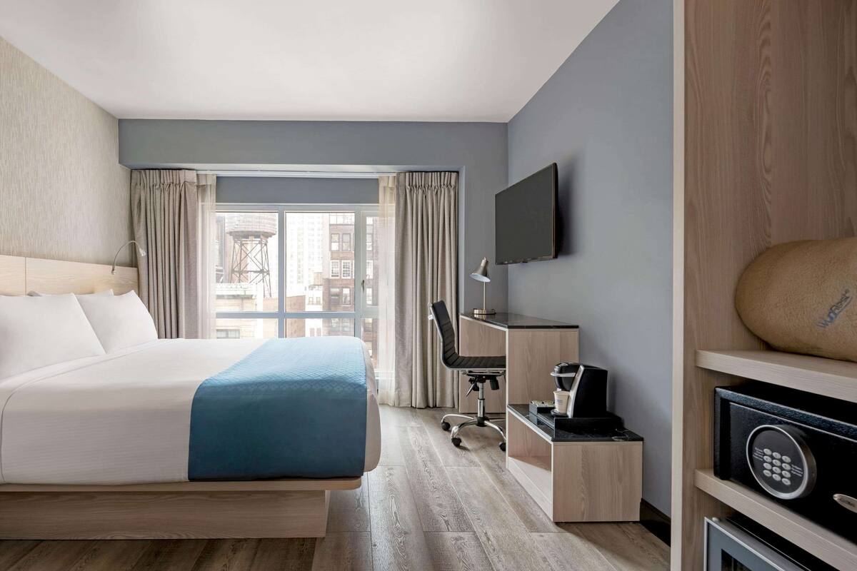 Une chambre d’hôtel équipée d’un lit, d’un bureau, d’une chaise, d’une télévision et offrant une vue sur la ville.