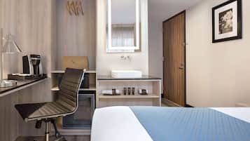 Habitación de hotel con cama, escritorio con silla, tocador con espejo, lavabo y armario.