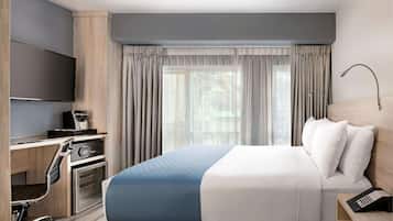 Habitación de hotel con una cama grande, un escritorio con computadora, una cafetera y un televisor montado en la pared.