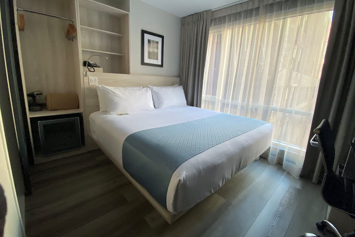 Une chambre d’hôtel avec un grand lit, une armoire, un bureau et une fenêtre avec des rideaux.