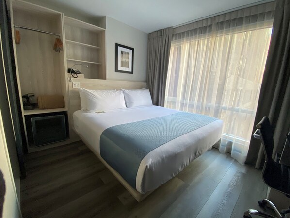 A hotel room with a large bed, a wardrobe, a desk, and a window with curtains.