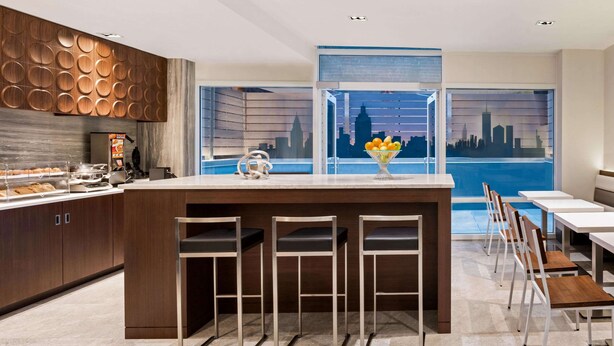 A modern kitchen with a central island, bar stools, and a cityscape view through large windows.