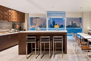 A modern kitchen with a central island, bar stools, and a cityscape view through large windows.