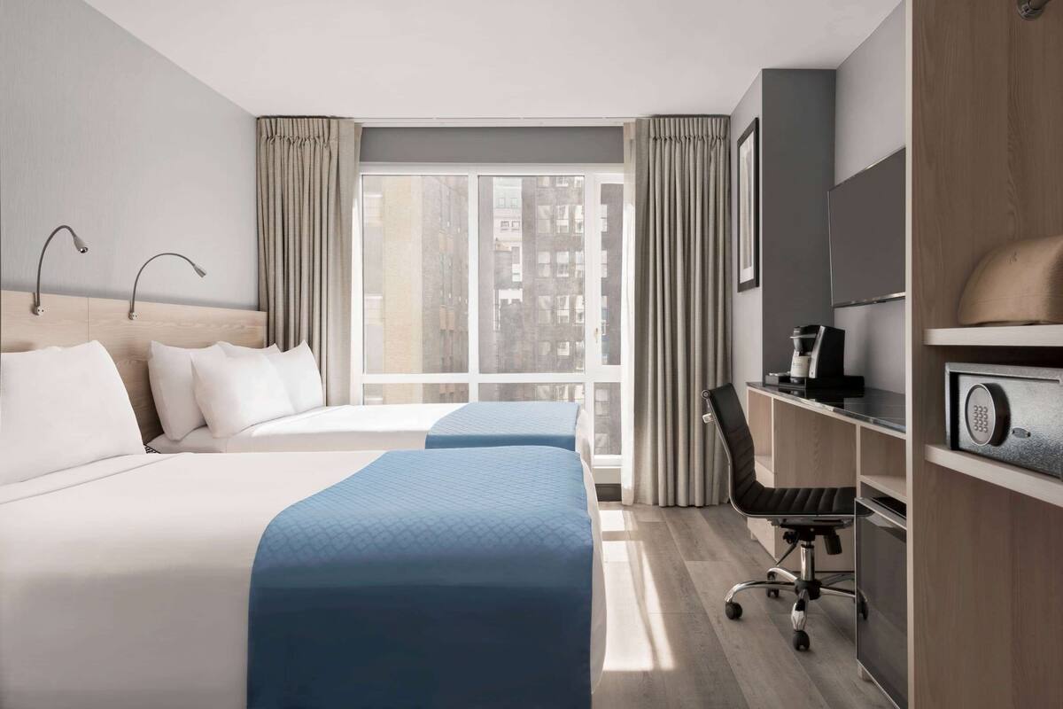 Une chambre d’hôtel avec deux lits, un bureau, une chaise, une télévision et une fenêtre avec des rideaux.