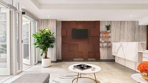 A modern living room with a large potted plant, a round coffee table, and a flat-screen TV mounted on a wooden panel wall.