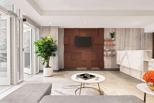A modern living room with a large potted plant, a round coffee table, and a flat-screen TV mounted on a wooden panel wall.
