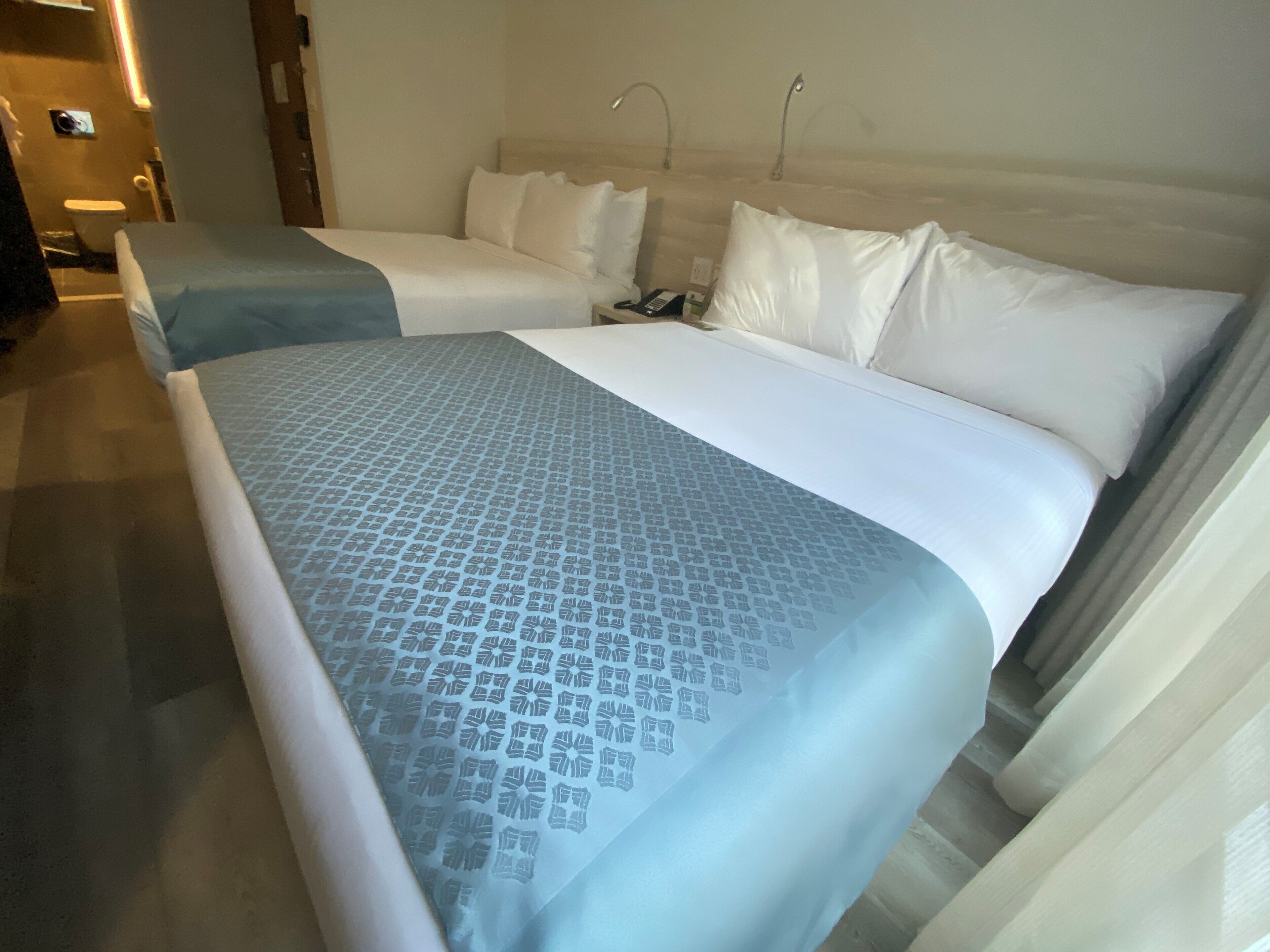 A hotel room with two beds, a nightstand, and a bathroom visible in the background.
