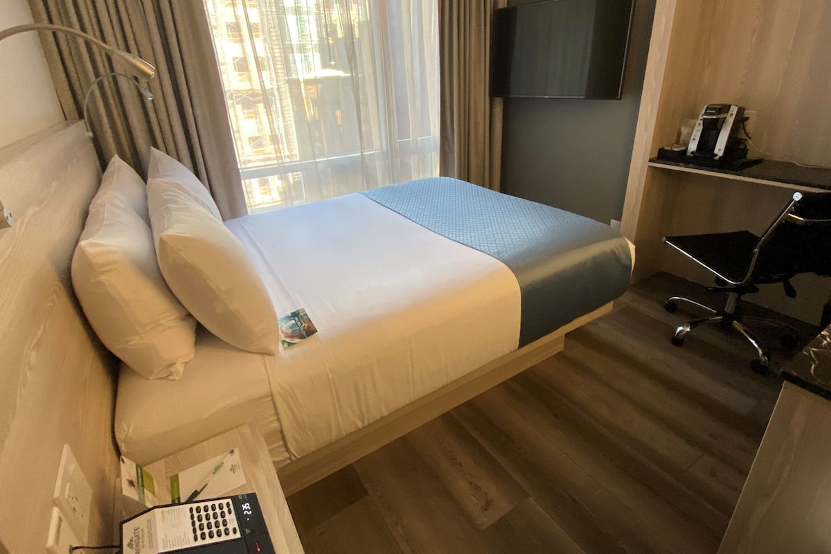 Une chambre d’hôtel avec un lit, un bureau, une chaise, une télévision et une fenêtre avec des rideaux.