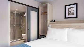 Quarto de hotel com chuveiro, cama, mesa de cabeceira e um quadro na parede.