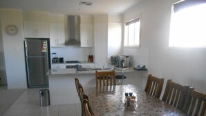 A modern kitchen with white cabinets, a stainless steel refrigerator, and a dining table with chairs. - The White House ~ Free Wi-Fi, Arcade Machine - Off Peak Special! (Edithburgh)