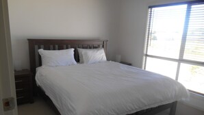 A bedroom with a wooden bed frame, white bedding, and a window with blinds. - The White House ~ Free Wi-Fi, Arcade Machine - Off Peak Special! (Edithburgh)