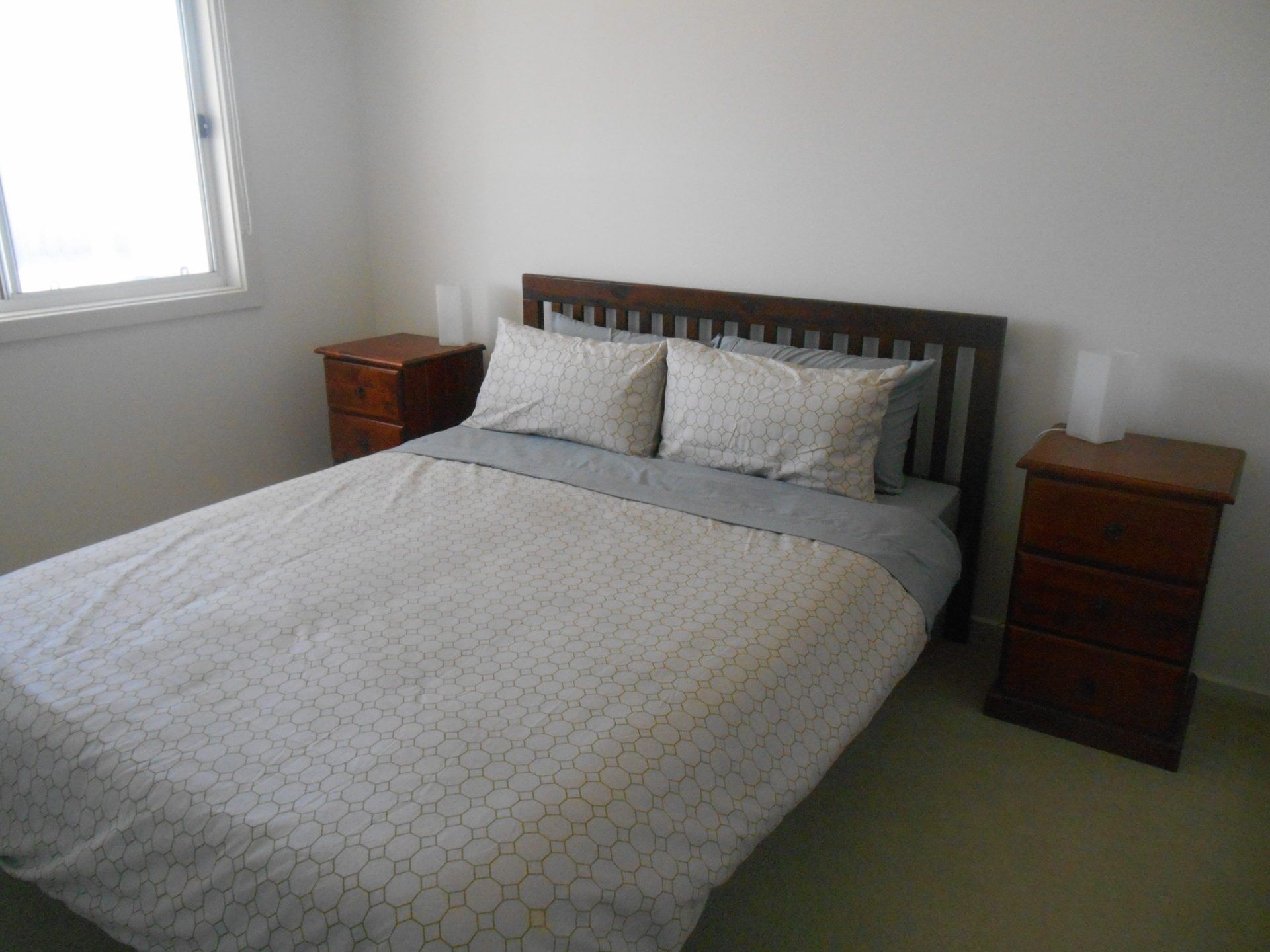 A bedroom with a bed, two nightstands, and a window.
