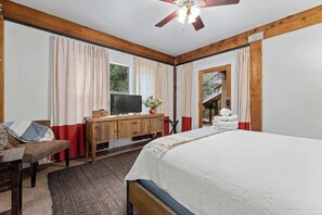 Une chambre à coucher comprenant un lit, une commode en bois, une télévision et donnant sur un escalier menant à l’extérieur.