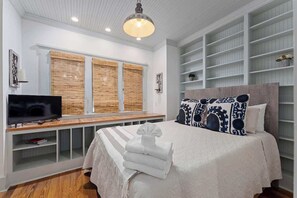 Une chambre à coucher avec un lit, une télévision, une étagère remplie de livres et une fenêtre avec des stores.