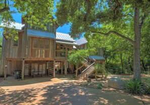 Une grande maison en bois, avec un toit en métal, entourée d’arbres et bordée d’une allée pavée.