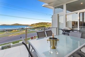 Een balkon met een glazen tafel, een champagnefles en twee glazen.