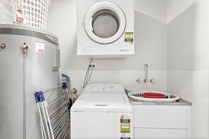 A laundry room with a front-loading washing machine, a dryer, and a utility sink. - Serenity 1 at Fingal Bay with Ocean Views (Fingal Bay)